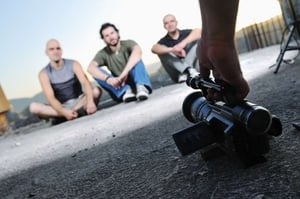 three young man siting on ground while modern video camera recording